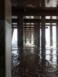 Concrete and metal architectural pillars supporting a fishing pier with incoming water.