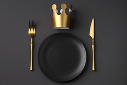 Festive creative royal table setting on a dark background. Gold crown, fork and knife. Valentine's Day, Wedding Day, Birthday, Women's Day and Mother's Day. Flat lay