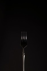 Stylish steel black fork on a dark background. Close-up. Monochrome. Vertical position. Copy space