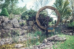 Water wooden old wheel mill in country village near pond stream. Retro vintage machinery in idyllic rustic rural country-side.
