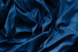 Closeup classic blue macro texture of shiny smooth material fabric or clothing. Toned trendy 2020 year color background with wrinkles and folds. Dark blue monochrome backdrop wallpaper. 