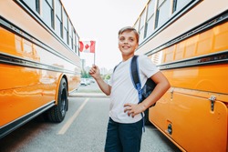 Caucasian boy student holding Canadian flag. Happy smiling student kid near yellow school bus in Canada. Education and back to school in September. 