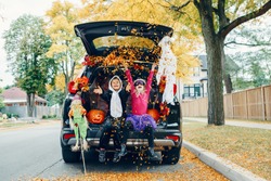 Trick or trunk. Children celebrating Halloween in trunk of car. Boy and girl with red pumpkins celebrating traditional October holiday outdoor. Social distance during coronavirus pandemic.