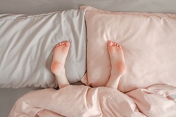 Kids child legs feet lying on pillows in bed at home. Child playing hide and seek game under blanket. Pink cute adorable baby heels upside down in bed. Happy authentic childhood lifestyle.