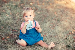 Toddler baby eating baby food organic vegetable fruit puree from pouch. Supplementary solid healthy food meal snack for babies kids. Girl eating outdoor in park on summer day. 