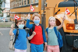 Proud happy students children with face masks holding Canadian flags. Education and back to school of kids classmates in September. New normal during coronavirus covid-19 in Canada. 