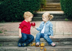 Group portrait of two white Caucasian cute adorable funny children toddlers sitting together sharing apple food, love friendship childhood concept, best friends forever
