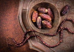 Arabian dates in an antique metal bowl with Islamic prayer beads. Ramadan Kareem- Muslim festival objects and background.
