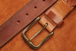 Brown leather belt with bronze buckle on chamois leather background texture. Man fashion concept. Top close up view.