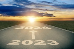 Asphalt road with white arrow sign and 2024 text goes to horizon. Sunshine on horizon and the road strigt away forward. Moving forward into new year concept. Clear and positive perspectives ahead.