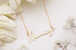 Gold necklace with name inscription displayed on a floral background. Jewelry photo for e-commerce, online sale, social media.