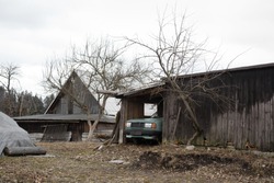 Authentic yard in poor Eastern Europe. Old wooden cottage and retro vintage car is in the barn. Abandoned and desolated vehicle. Nostalgia of ugly fall / winter. Bare tree (low depth of field)