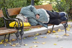 Homeless person is sleeping on a bench in a cold autumn day in a park in European union's poorest country Bulgaria.
