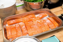 Metal tray with raw salmon fillets under coarse salt. Salted before cooking.
