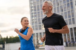 Portrait of active middle aged couple, man and woman in sportswear looking happy while jogging together outdoors, having mroning workout