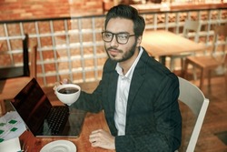 Handsome businessman in suit drinking coffee in cafe during break time sitting near window