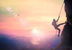 Adventure concept: Silhouette bold heroic man try to climb with rope over natural rocky wall wide valley autumn sunset mountain background