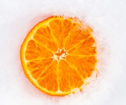 A slice of fresh frozen orange tangerine mandarin fruit cowered with white cold winter snow