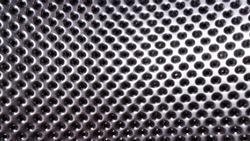 Shiny metal surface with lots of round holes. Perforated stainless metal. Fragment of a washing machine drum.