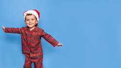 A studio shot of a happy boy in Christmas pajamas, fooling around and smiling. A place for your text. The concept of holidays.