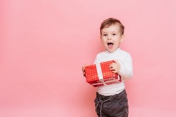 Gift in Hands Boy. Happy Baby Boy with Gift Box in Hands isolated on pink background.