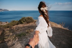 Follow me. A young girl in a white dress leads a man by the hand to the cliff. Look at her blue sea. The dress and hair are fluttering in the wind. The concept of freedom