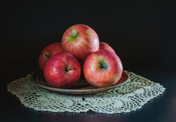 Big appetizing red apples on a clay plate on the table on a white napkin on a black background.