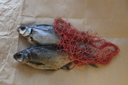 Two large dried bream for beer and a red string bag lie on a wooden board on craft paper