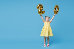Little child girl is holding foil balloons in the form of numbers 20 twenty percent. The concept of discounts, sales and cashback. Blue studio background