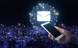 Email and sms marketing concept. Hand hold white smartphone with digital hologram Email and sms sign on city dark blurred background. Sending email.Bulk mail