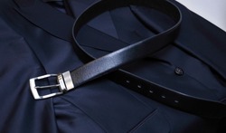 A black leather belt with steel fittings lies horizontally on a black men's jacket. An expensive gift option for men, premium leather, chic performance, handmade, exclusive. craft