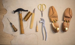 shoe tools, a hammer, wooden blocks, an awl, threads, scissors lie on a piece of leather, indoors. Shoemaker workplace, necessary tools, shoe repair, private business
