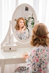 young woman is sitting in front of a mirror and smearing face cream. Women's room with dressing table