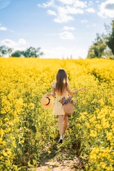 girl runs into a field of rapeseed. Yellow flower field. View from the back