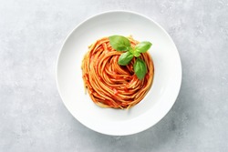 Top view of plate with spaghetti in tomato sauce and basil on white background