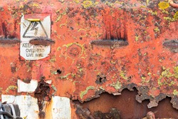 Rusted metal texture. Vintage machinery with warning sign, peeling paint and corroded metal, covered with yellow lichen