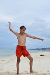 A boy in shorts on the beach waved his hand to throw a knife.