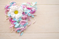 Love symbol on wooden background maid by blue and pink petals with daisy flower.