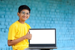 Technology concept : Cute indian little school boy using laptop and showing thumps up