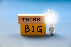 Think big text on wooden blocks with shining bulb on light blue background. Motivational concept