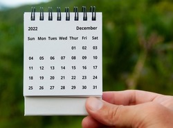 Hand holding December 2022 calendar with copy space and nature background.