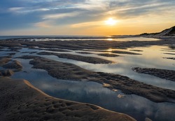Sand structures, trickles, small creeks and pools at low tide on Hörnum beach, Sylt island Germany. National Park “Wattenmeer“ with at sunset on a summer evening. Idyllic seascape on North sea coast.