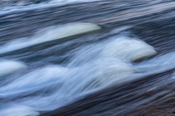 Water flowing quickly through a rapid cascade of high water Ruhr River in Witten Germany with waves, drops and splashes. Longtime exposure with motion and colorful water surface reflections.