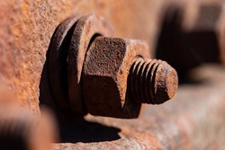 Rusty corroded iron screw with washer and thread on a railway profile in bright sunlight. Monochrome orange brown metal surface of a hex nut fixing. Macro close up with selective focus.