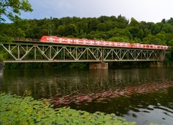 Historic green railway bridge spanning over Ruhr river in Essen-Kettwig Germany. Red multiple unit train from Düsseldorf to Essen passing steel construction with reflection on a rainy summer evening.