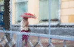 A woman silhouette with umbrella through wet window