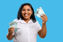 smiling dark-skinned woman holds 100 reais banknotes in hands, brazilian money, isolated on blue background