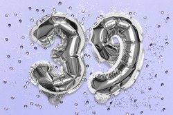 Silver foil balloon number, digit thirty nine on a lilac background with sequins. Birthday greeting card with inscription 39. Top view. Numerical digit. Celebration event, template.