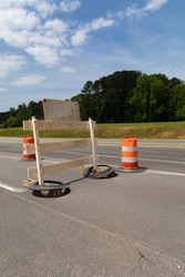 Rear view of traffic barricade and safety barrels, asphalt roadway copy space, blue sky and trees, vertical aspect