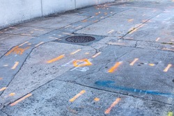 Heavily weathered sidewalk with spray painted indicators of buried utility features, manhole cover, horizontal aspect